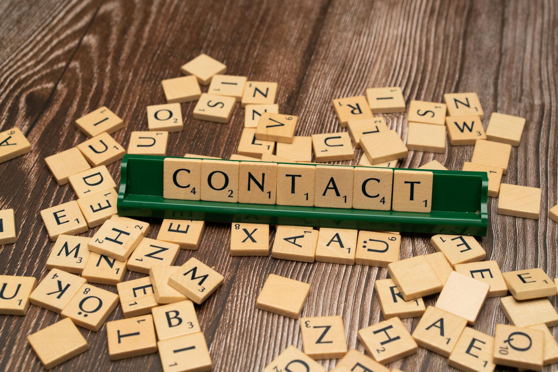 Scrabble tiles spelling CONTACT on a wooden surface